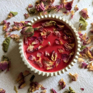 Bougie pétales de rose en cire de soja rouge dans un bougeoir en plâtre blanc, entourée de pétales séchés
