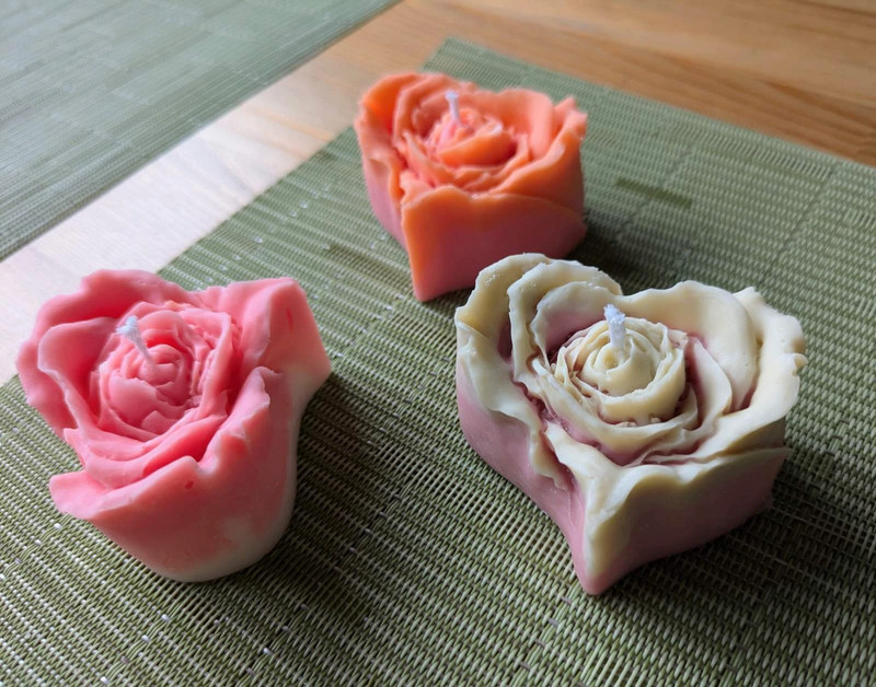Trois bougies rose cœur, rose vif, orange et crème, sur un set de table vert