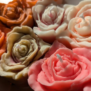 Bougie rose cœur en cire de soja, plusieurs fleurs orange, pêche, crème et rose vif posées sur du bois