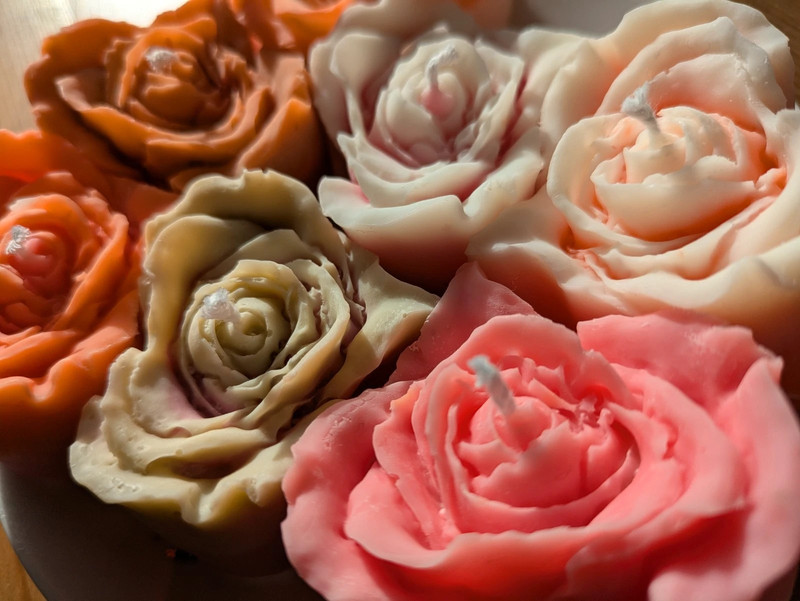 Bougie rose cœur en cire de soja, plusieurs fleurs orange, pêche, crème et rose vif posées sur du bois