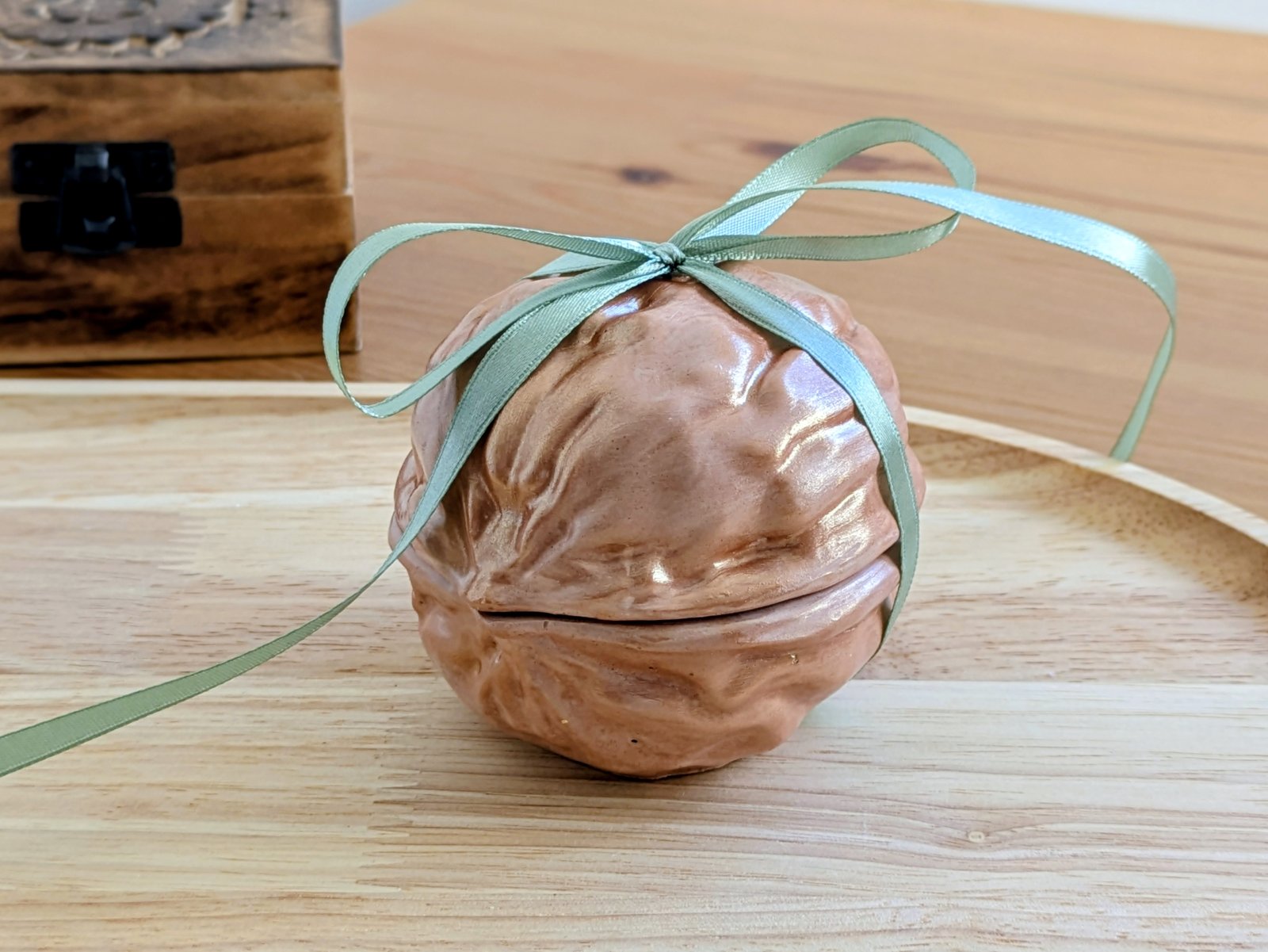 Noix décorative en plâtre nouée d'un ruban vert devant un coffret en bois