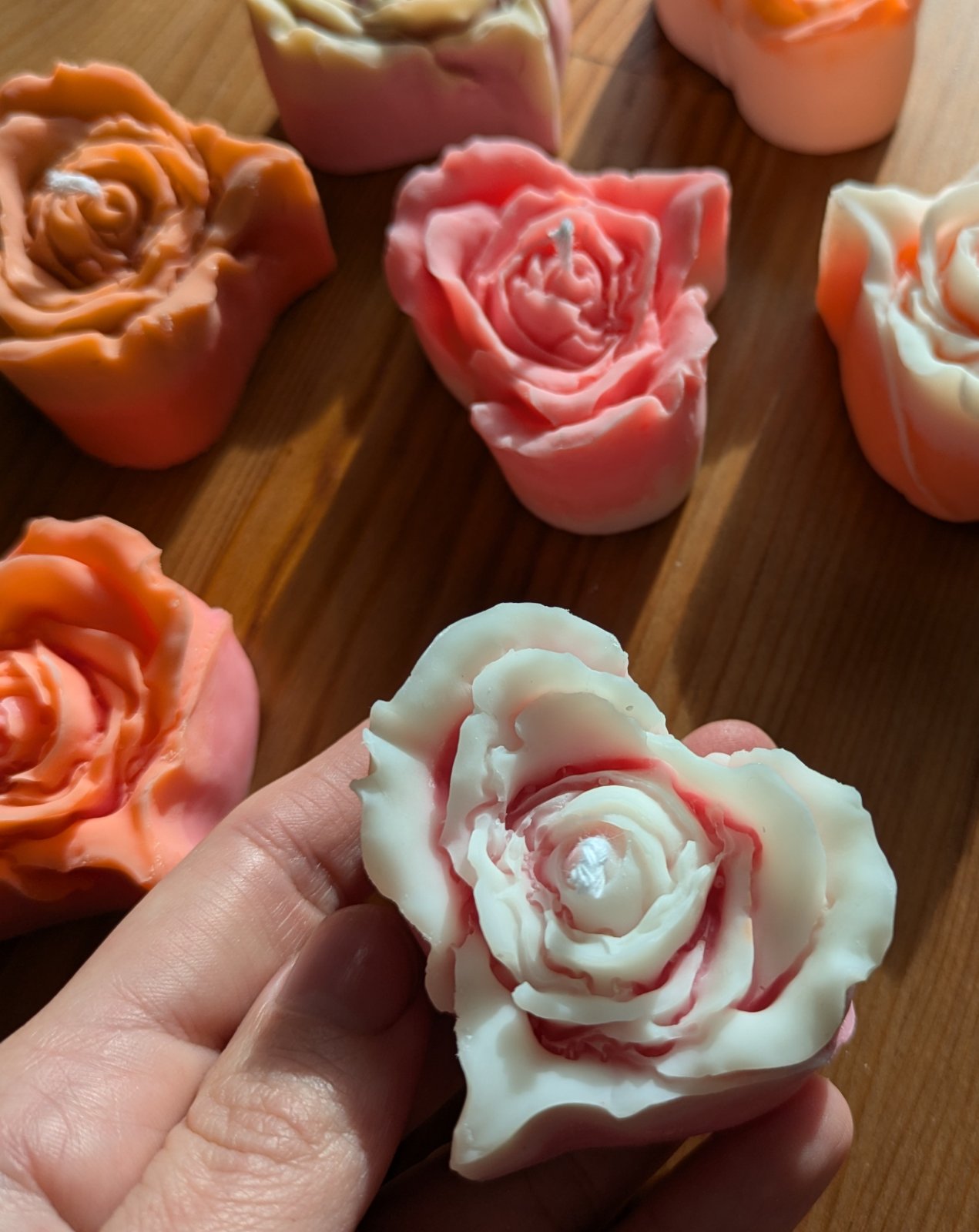 Bougie rose cœur crème marbrée de rose tenue dans la main, autres fleurs colorées autour