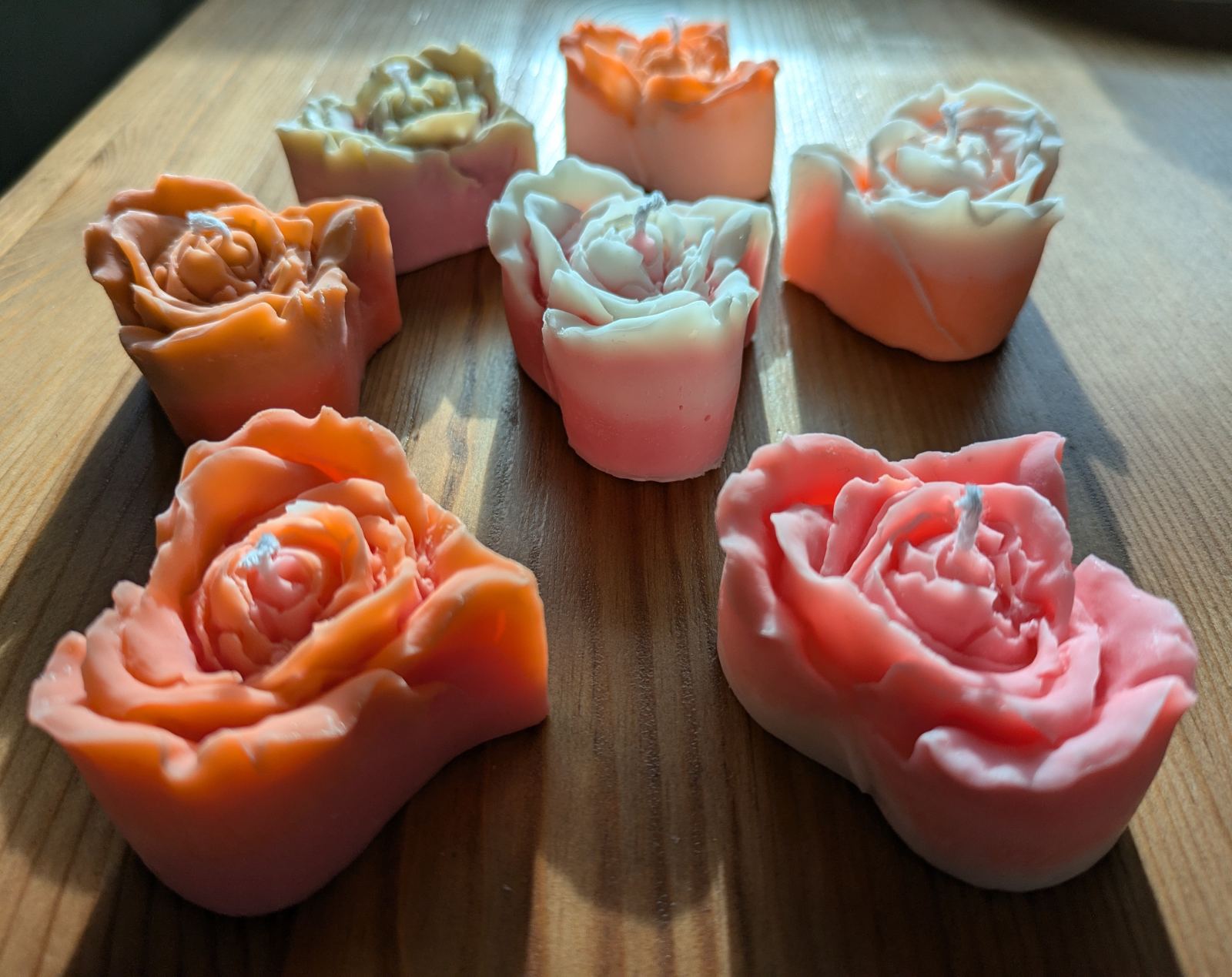 Six bougies rose cœur en cire de soja, orange, rose vif, pêche et crème, sur une table en bois