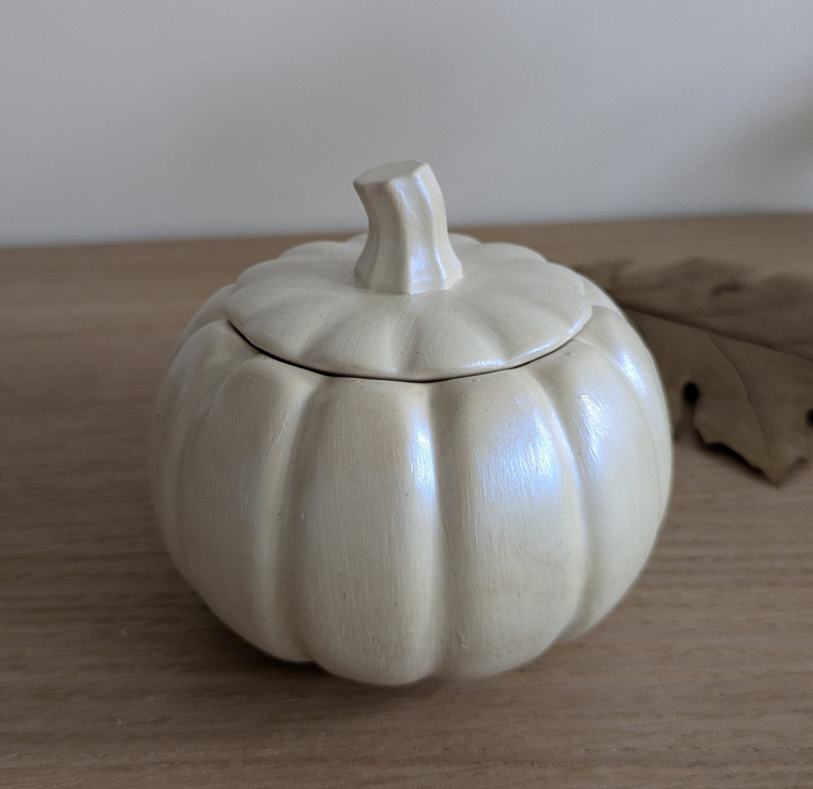 Bougie citrouille nacrée à couvercle posée sur une table en bois, reflets de perle
