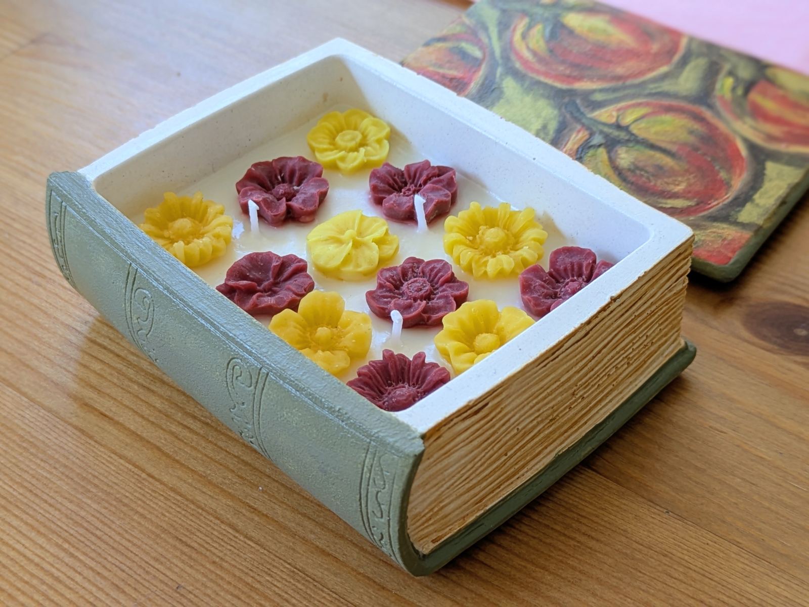 Grande bougie livre ouverte sur une table en bois, douze fleurs de cire et trois mèches