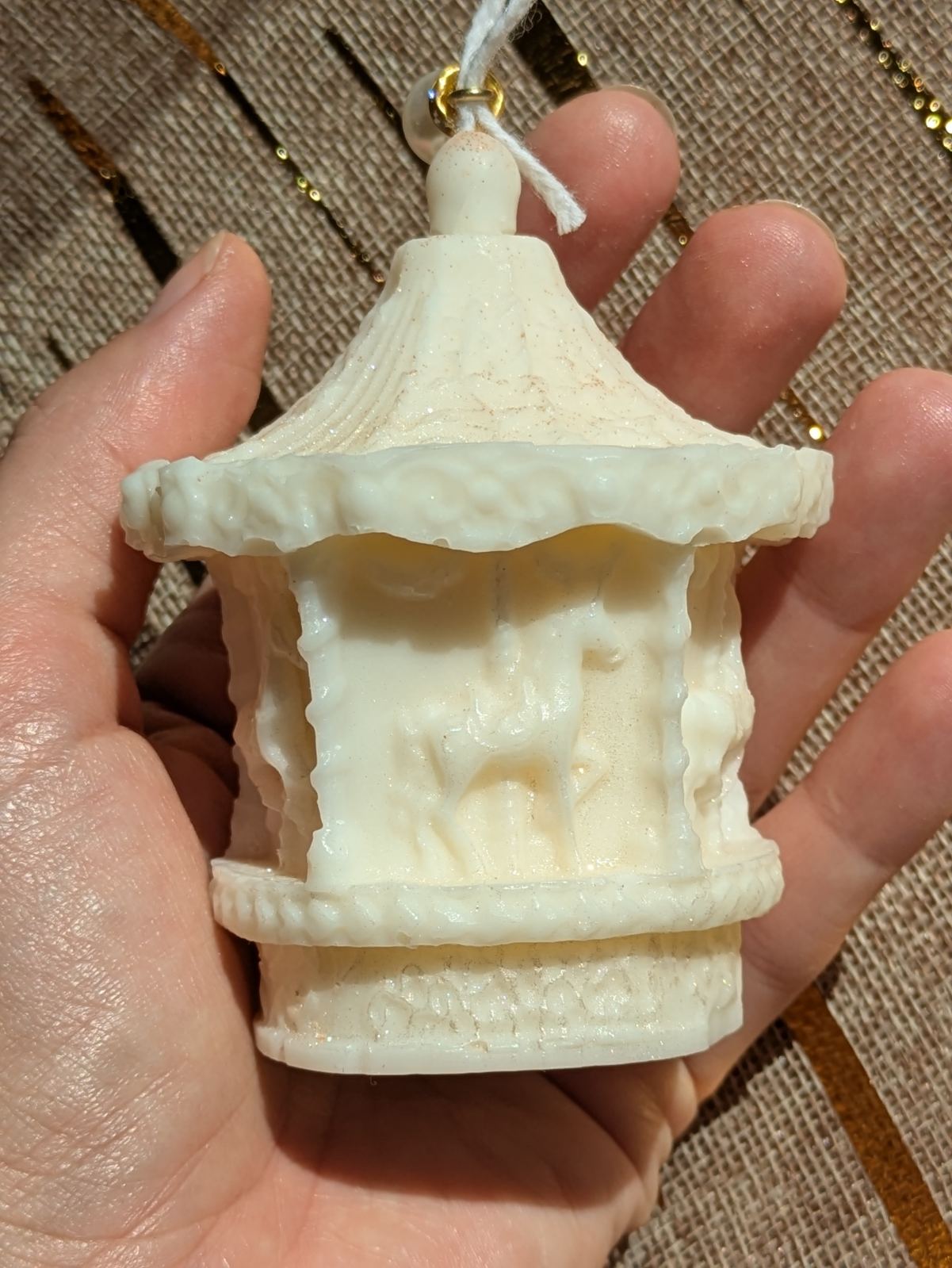 Bougie manège beige crème tenue dans la main, chevaux de bois en relief