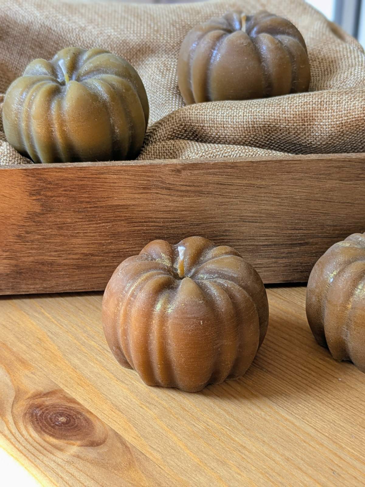 Bougie citrouille poudre dorée aux reflets cuivrés devant un plateau en bois et de la toile de jute