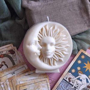 Bougie lune et soleil ivoire aux visages sculptés, posée sur des cartes de tarot