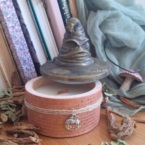Bougie chapeau de sorcier rose en plâtre, tour de briques et pendentif citrouille, devant des livres