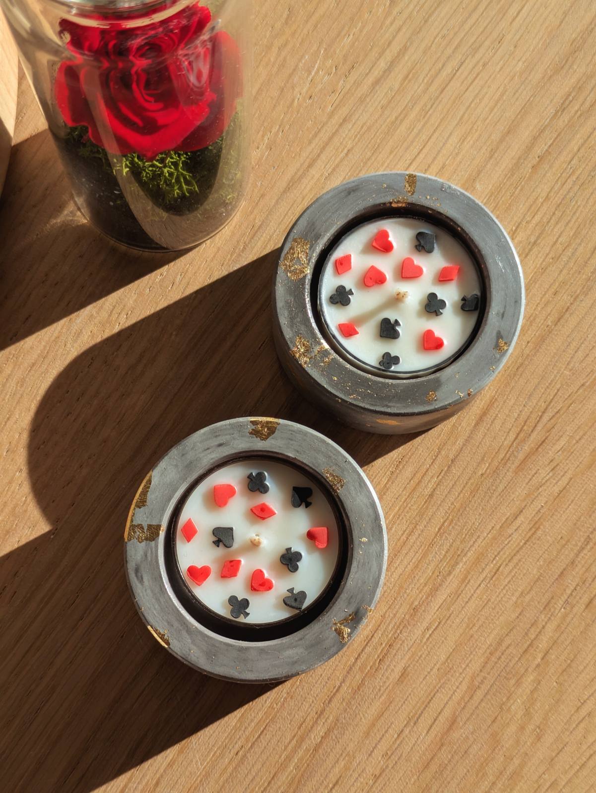 Bougie cartes à jouer dans son bougeoir gris au soleil, à côté d'une rose sous cloche