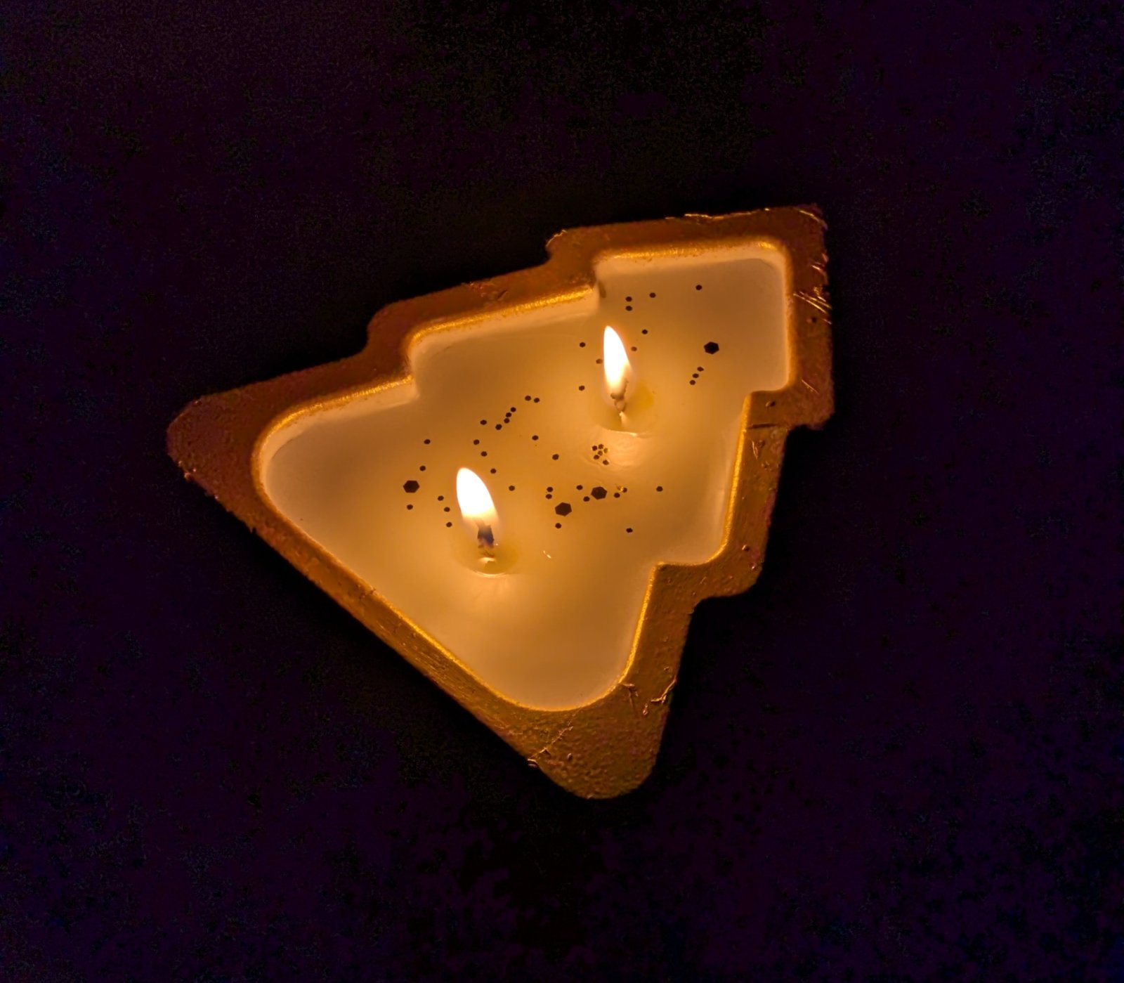 Bougie sapin de Noël allumée dans le noir, flammes et lueur dorée sur le bougeoir